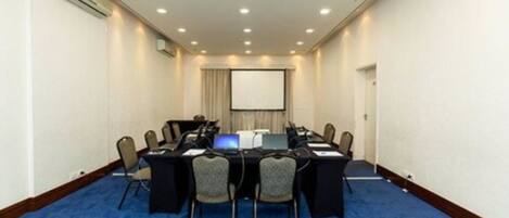 Un salón de conferencias con una larga mesa, sillas, computadoras portátiles y una pantalla de proyector.