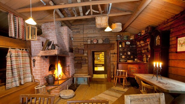 Ein rustikales Blockhaus-Interieur mit Kamin aus Ziegelsteinen, Holzmöbeln und einer Sammlung alter Dinge auf Regalen.