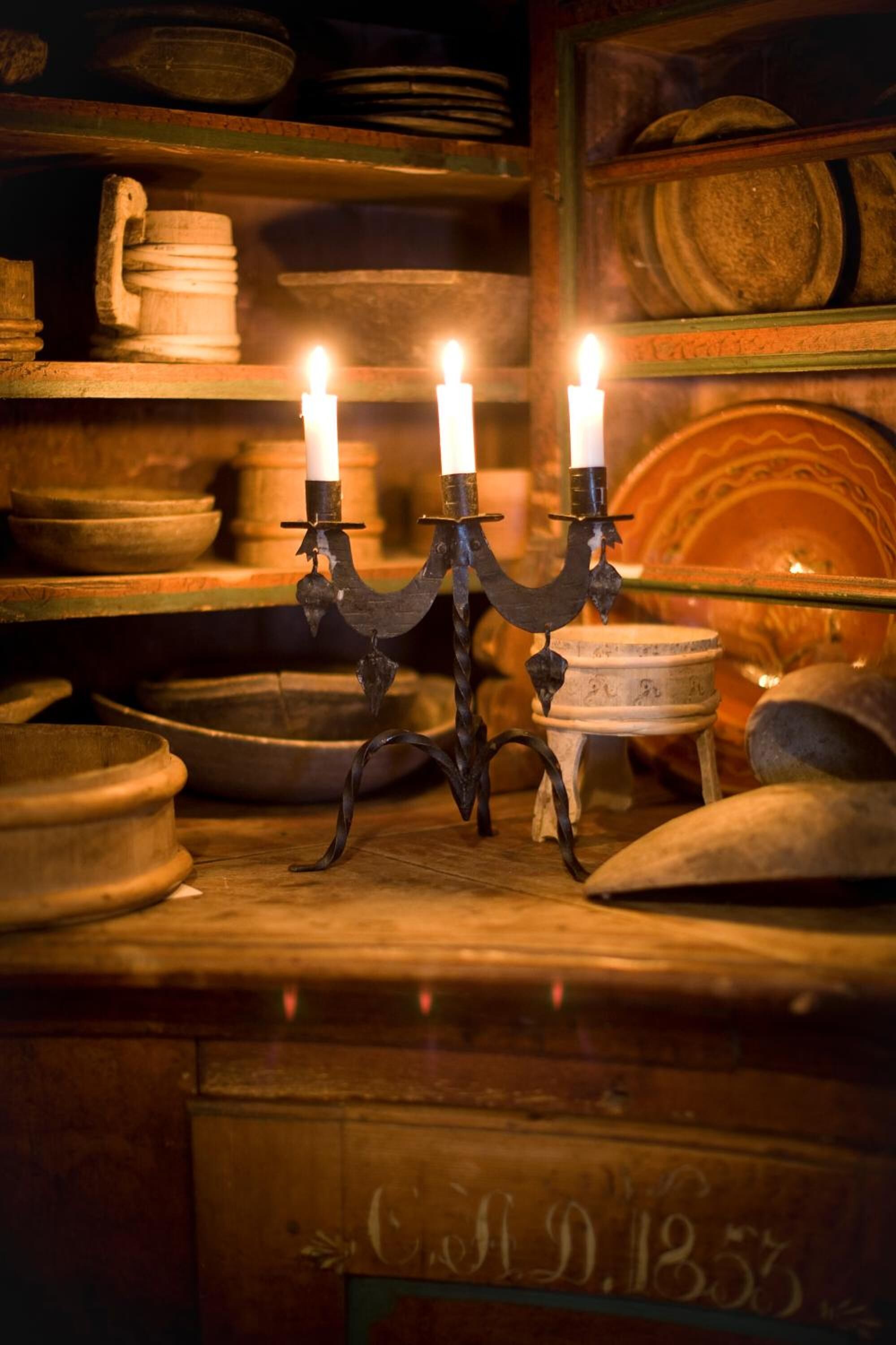A candelabra with two lit candles, surrounded by various pottery items on shelves.