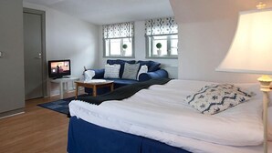 Ein Schlafzimmer mit einem Bett, einem Schreibtisch mit Computer, einer Lampe und einem Fenster mit Vorhängen.