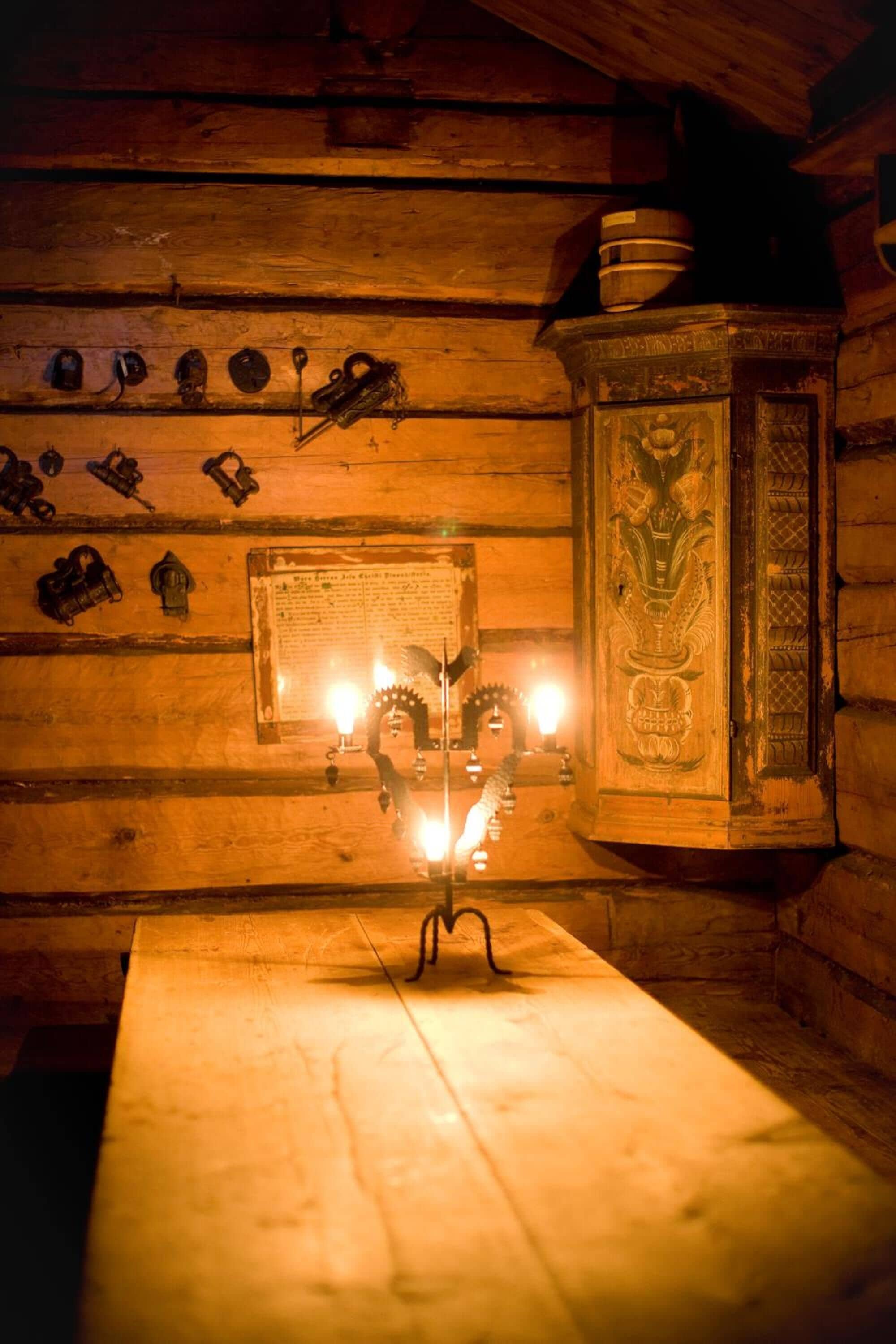 En stuga med träpanel på insidan, med ett bord, väggmonterade krokar och ett dekorativt skåp.