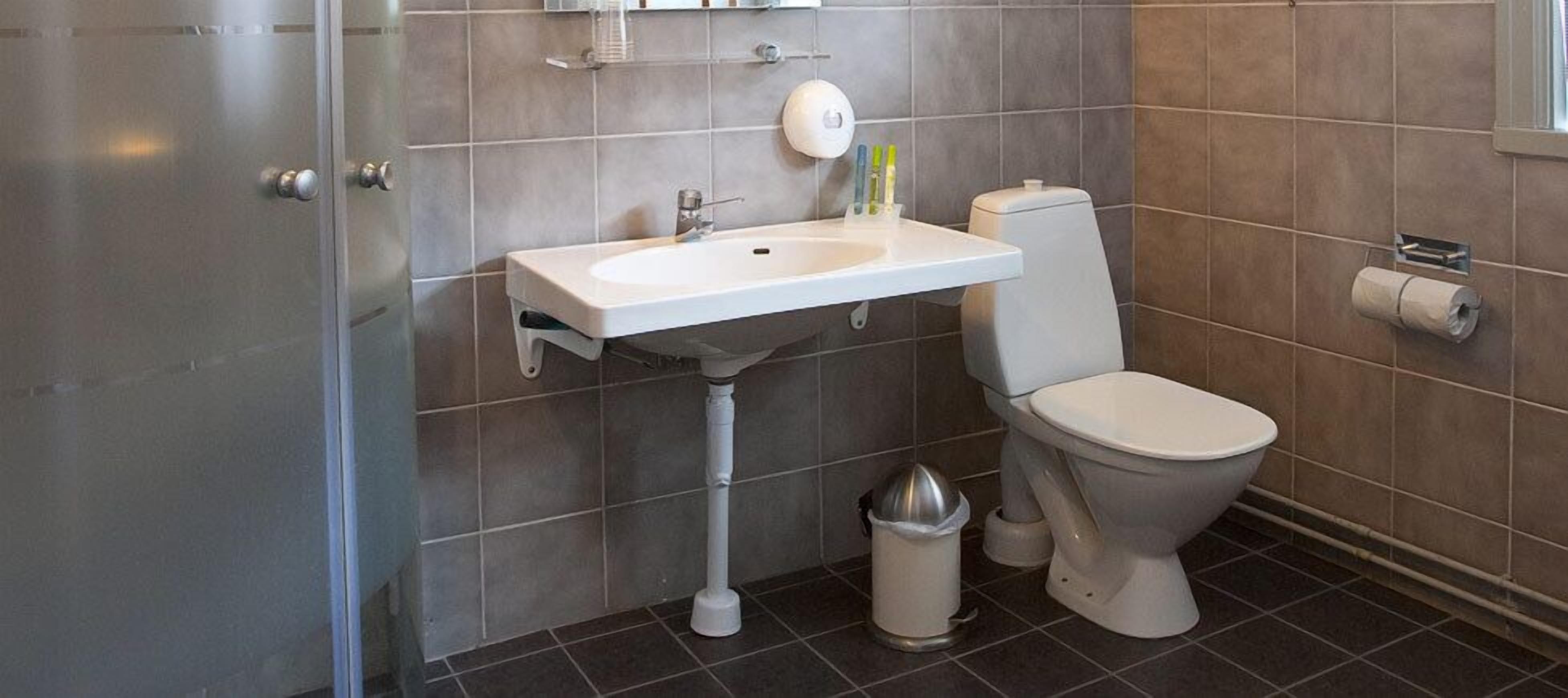 A bathroom with a white sink, toilet, and a trash bin.