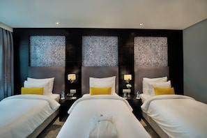 A hotel room with two beds, a dark wall with intricate patterns, bedside tables with lamps, and a small vase with flowers.