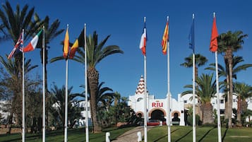 A building with a prominent 'RIU' sign, surrounded by palm trees and multiple flags.