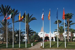 A building with a prominent 'RIU' sign, surrounded by palm trees and multiple flags.