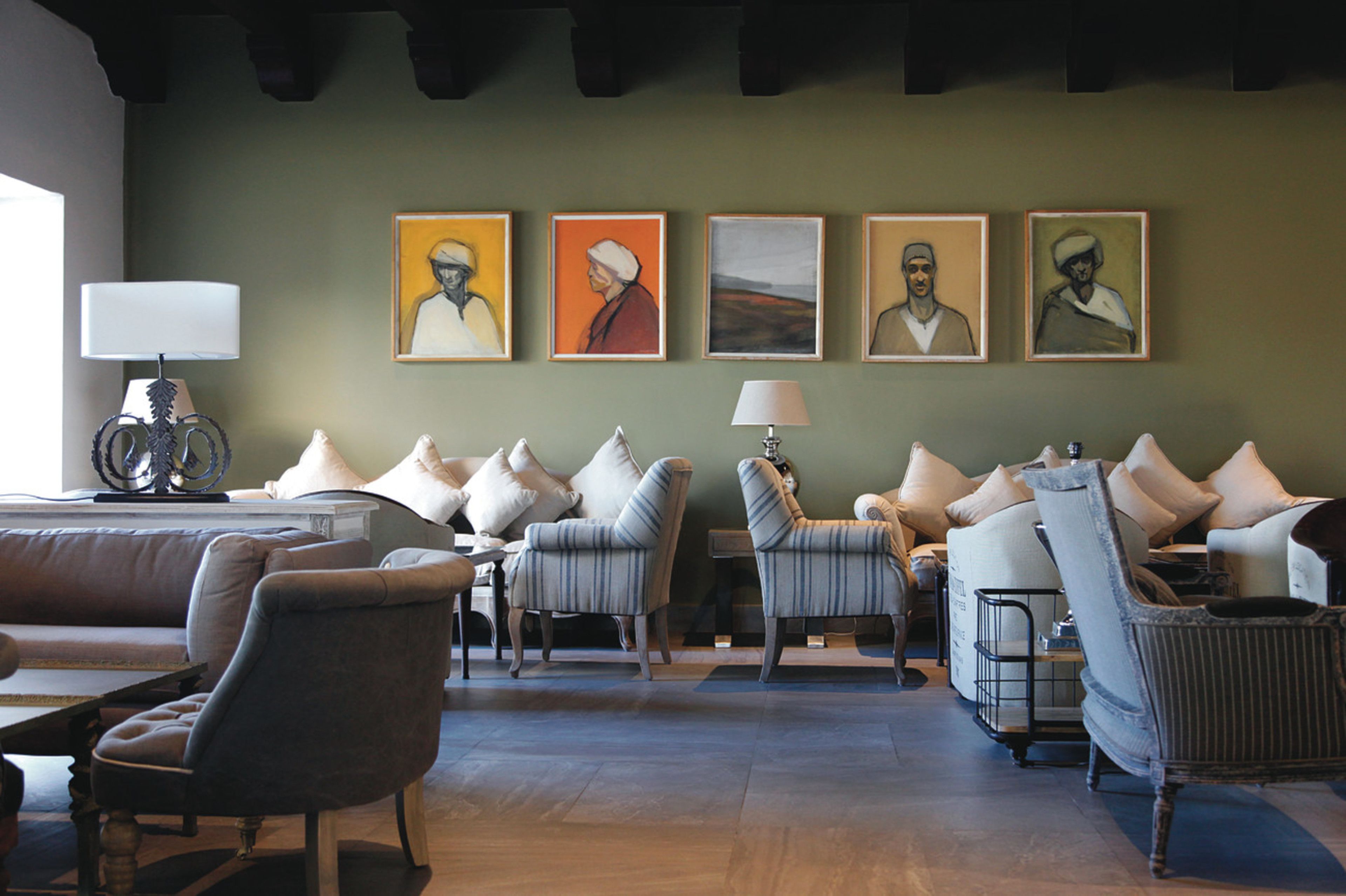 Een moderne woonkamer met een bank, fauteuils en een salontafel. Er hangen ingelijste kunstwerken aan de muur en op de bijzettafel staat een lamp.