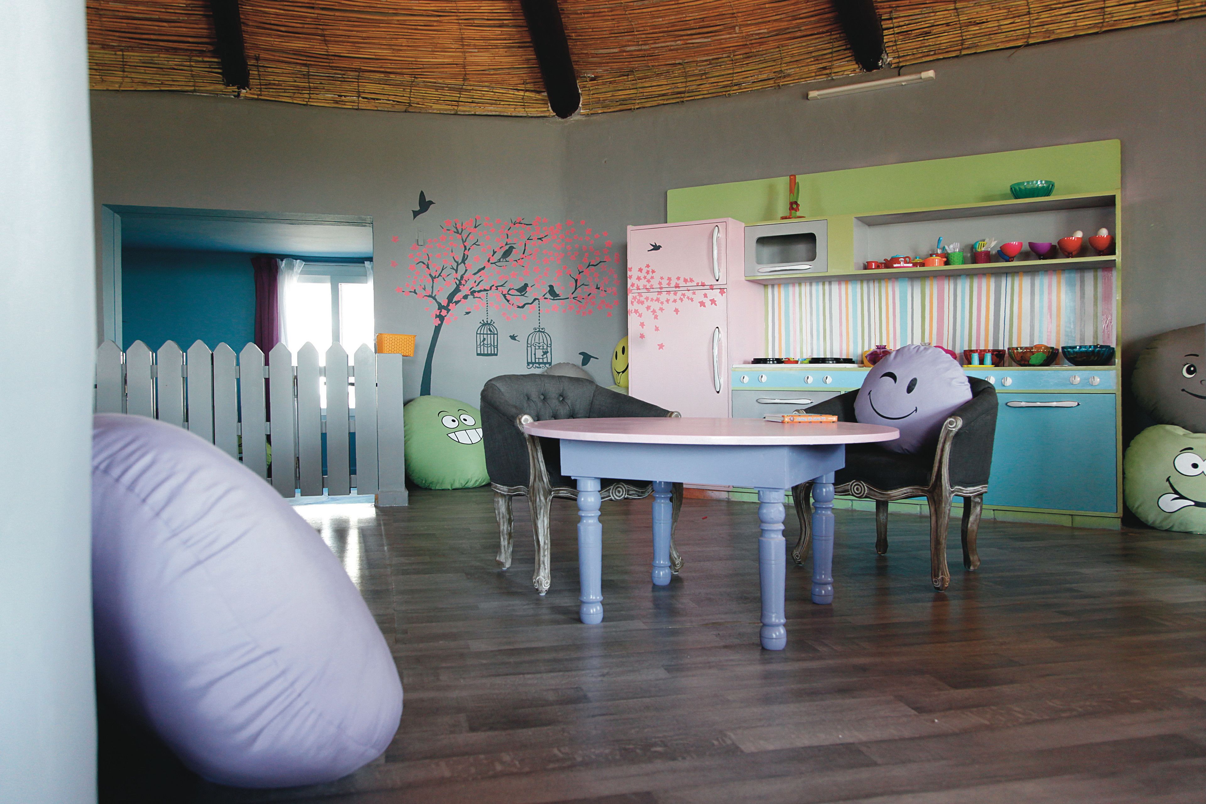 Ein Kinderzimmer mit Esstisch, Stühlen, einem pinken Kühlschrank und einer Wand, die mit einem Baum und Vögeln verziert ist.