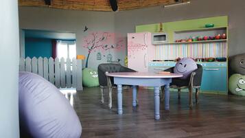 A child's playroom with a dining table, chairs, a pink refrigerator, and a wall decorated with a tree and birds.