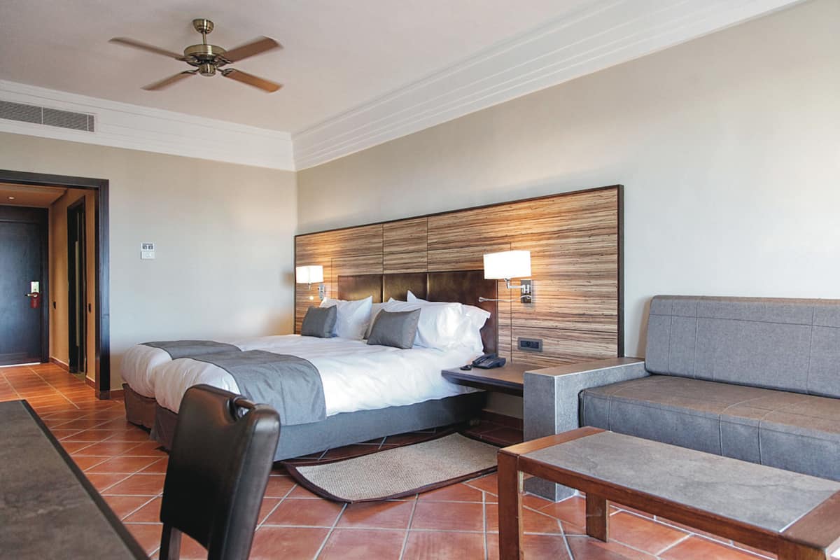 Une chambre d’hôtel équipée d’un lit, d’un canapé, d’une chaise, d’une table de chevet et d’un ventilateur de plafond.