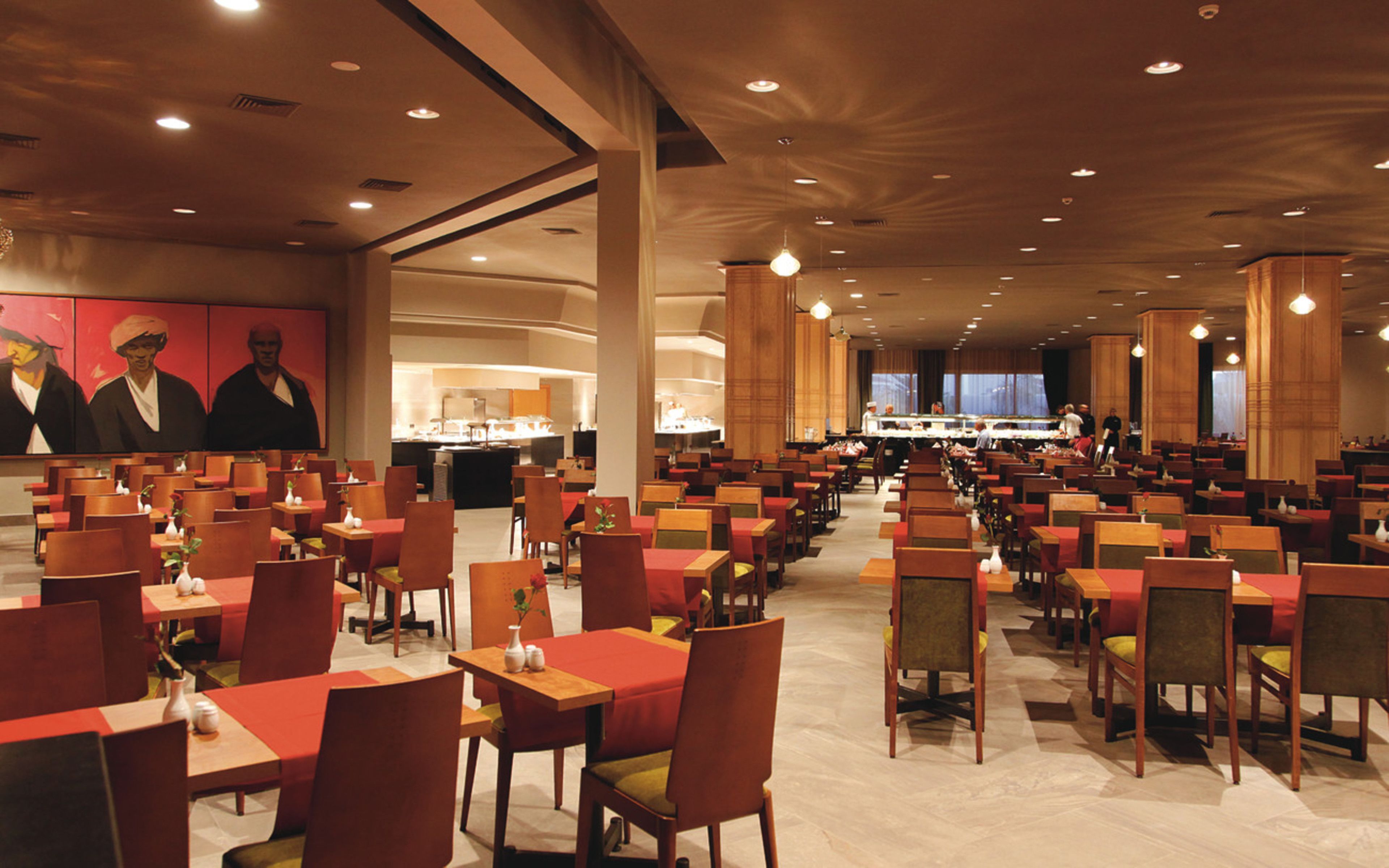 A spacious dining area with multiple tables and chairs, a buffet line, and a large mural on the wall.