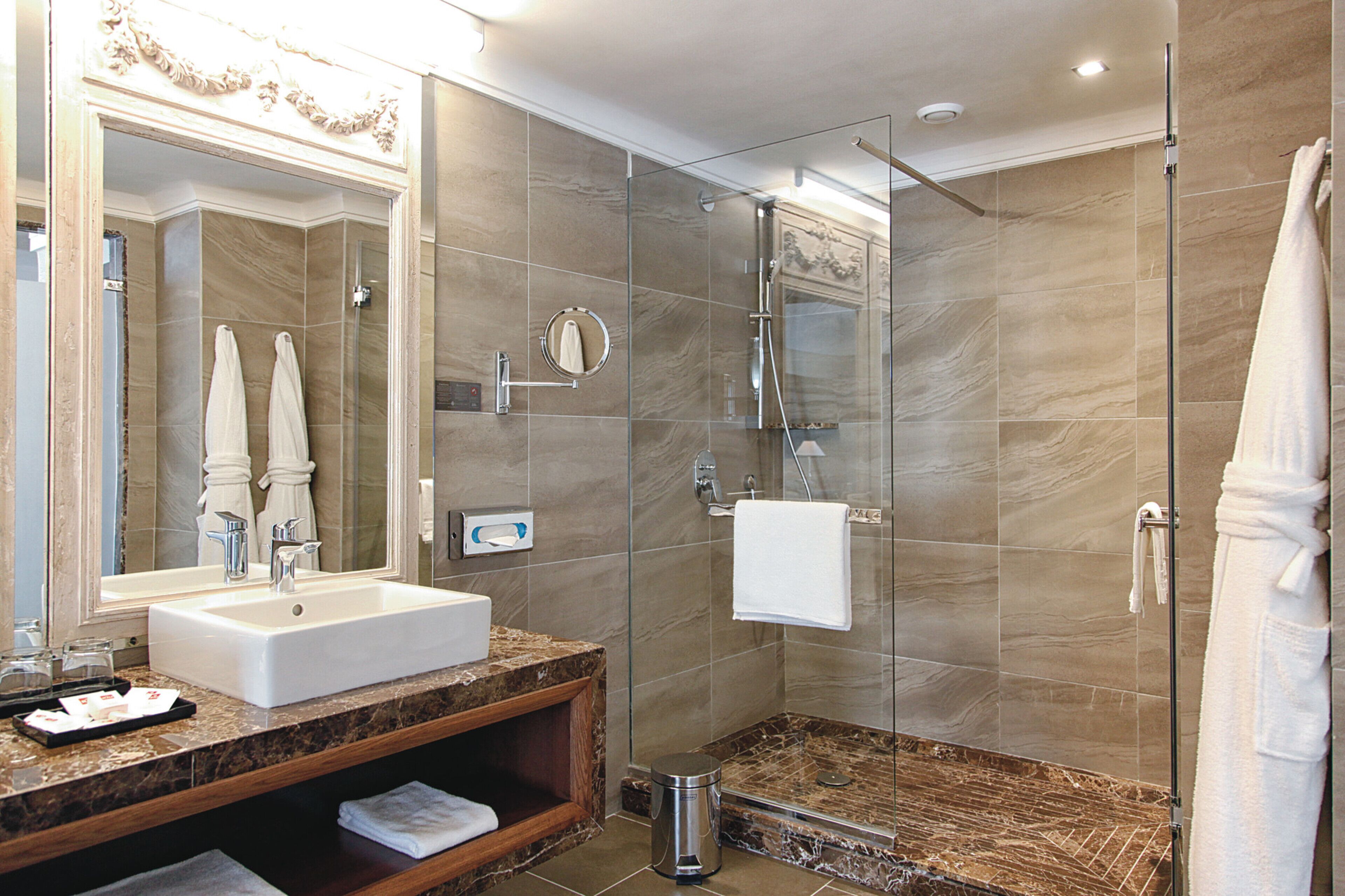 A modern bathroom with a marble sink, a glass-enclosed shower, and a large mirror.
