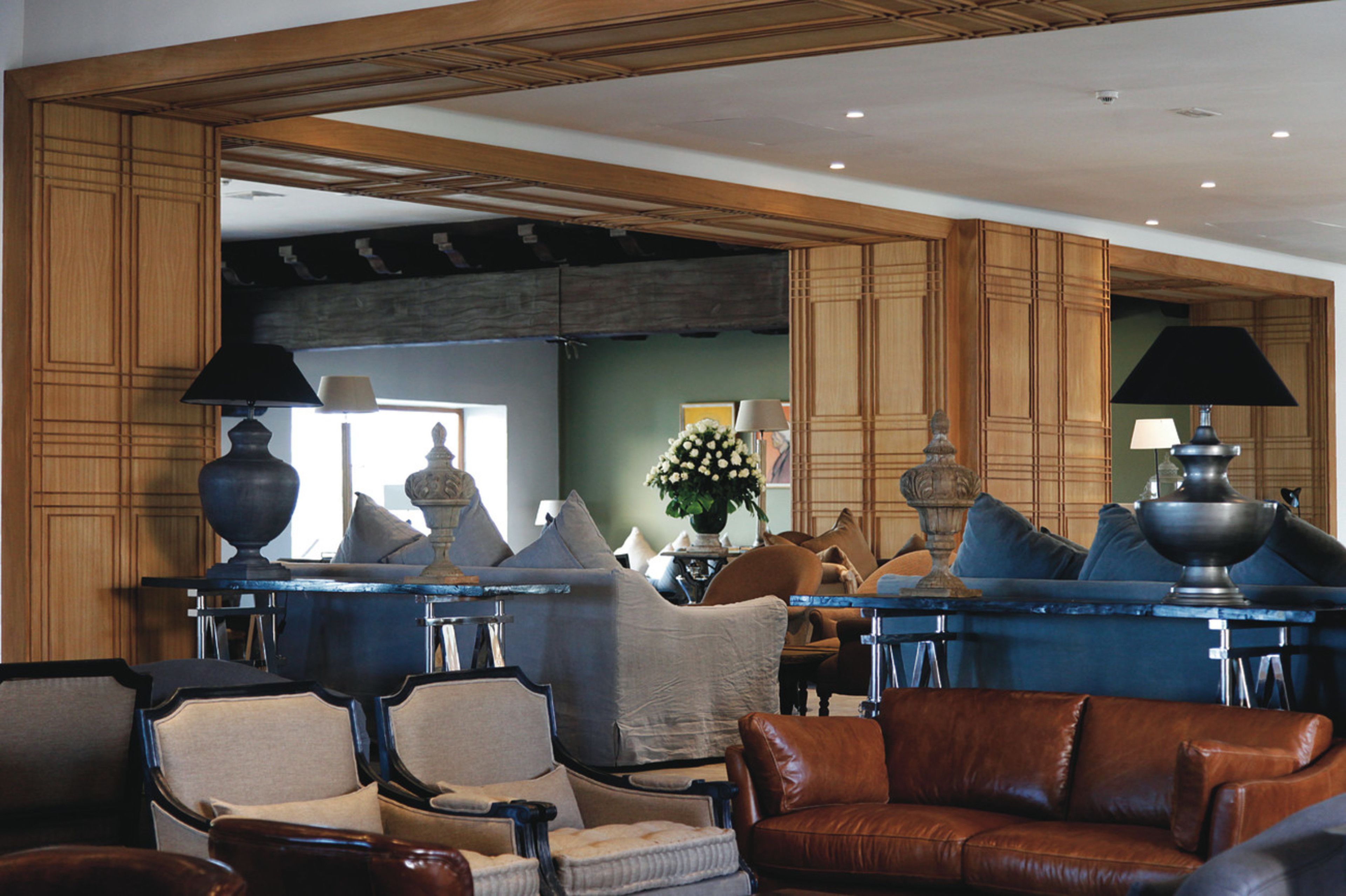 A spacious living room with a high ceiling, wooden paneling, and a variety of seating including a brown leather sofa, armchairs, and a chaise lounge.