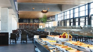 A buffet area with various food options, seating arrangements, and a large windowed wall in the background. - Hotel Riu Tikida Dunas - All Inclusive (Agadir)