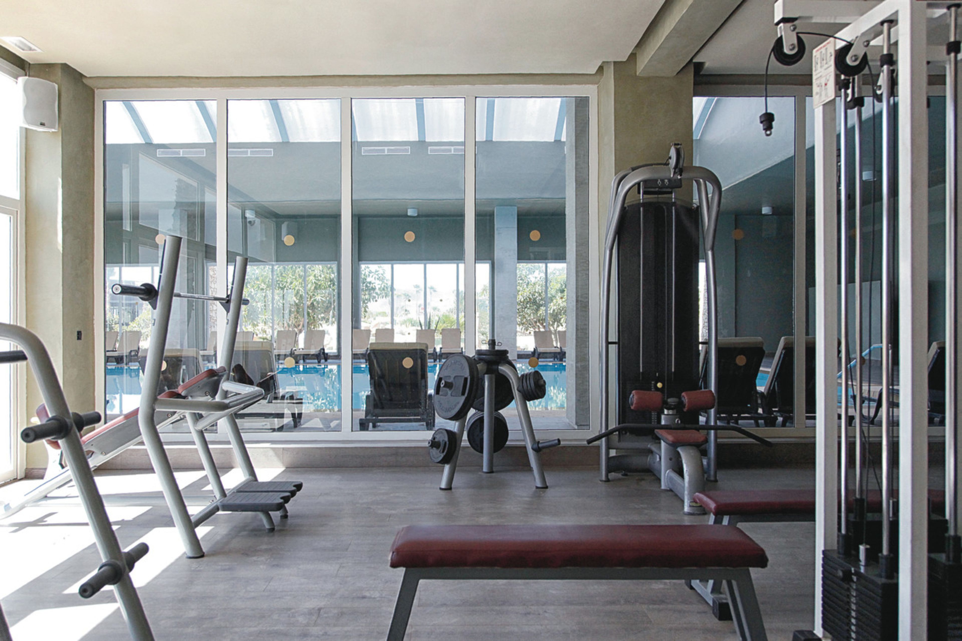 A gym with exercise equipment, a bench, and a view of a pool through large windows.
