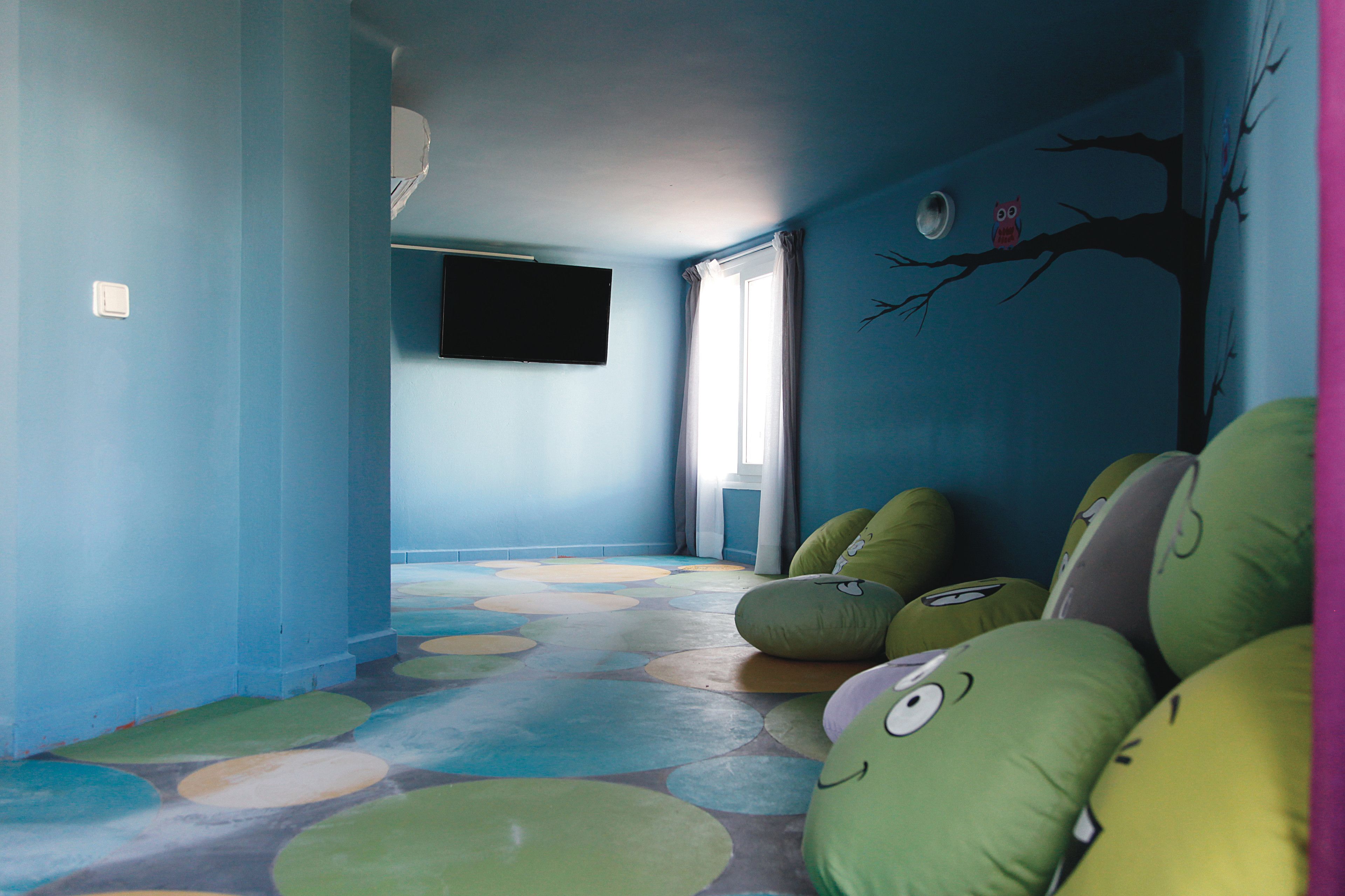 Una habitación con pared azul, un mural de un árbol y pufs.