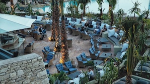 An outdoor lounge area with multiple seating arrangements, including sofas and chairs, surrounded by palm trees and plants. - Hotel Riu Tikida Dunas - All Inclusive (Agadir)