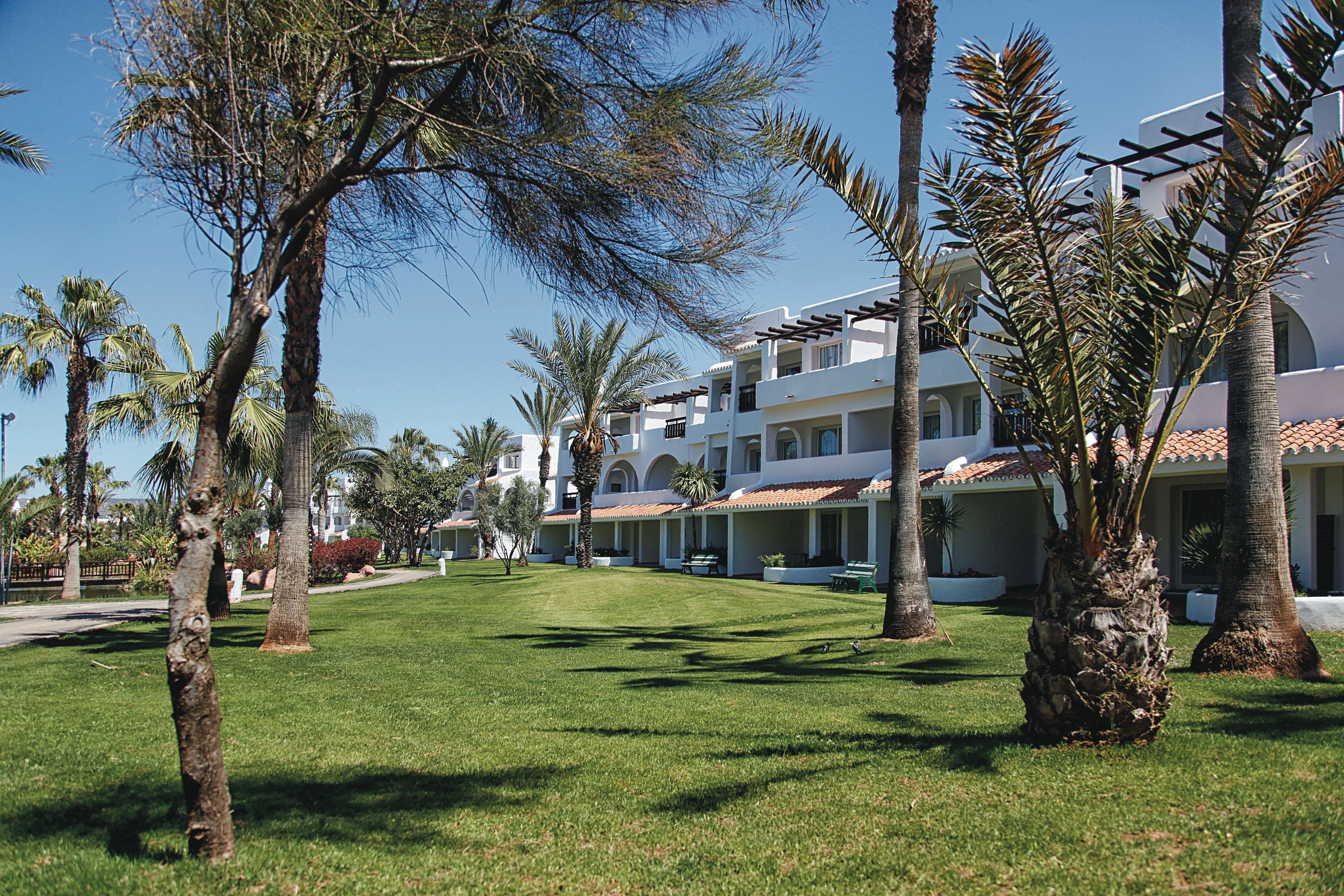 A resort with multiple-story buildings, palm trees, and a well-maintained lawn.