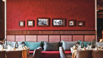 Een restaurantinterieur met een rode bekleden zithoek met een bank, een muur versierd met ingelijste foto's en gedekte tafels.