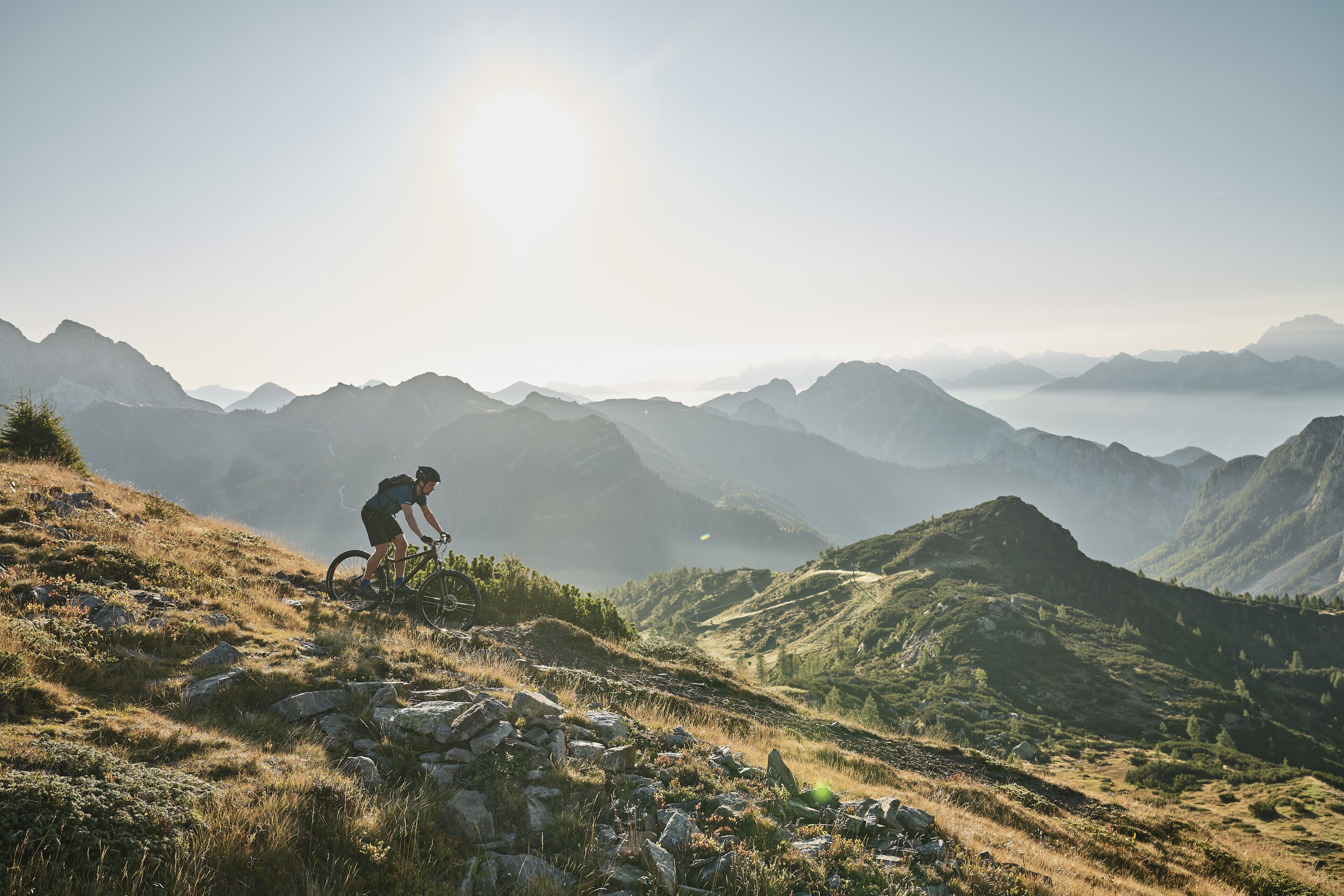 En mountainbikecyklist på en stig med en vidsträckt utsikt över avlägsna berg och en klar himmel.