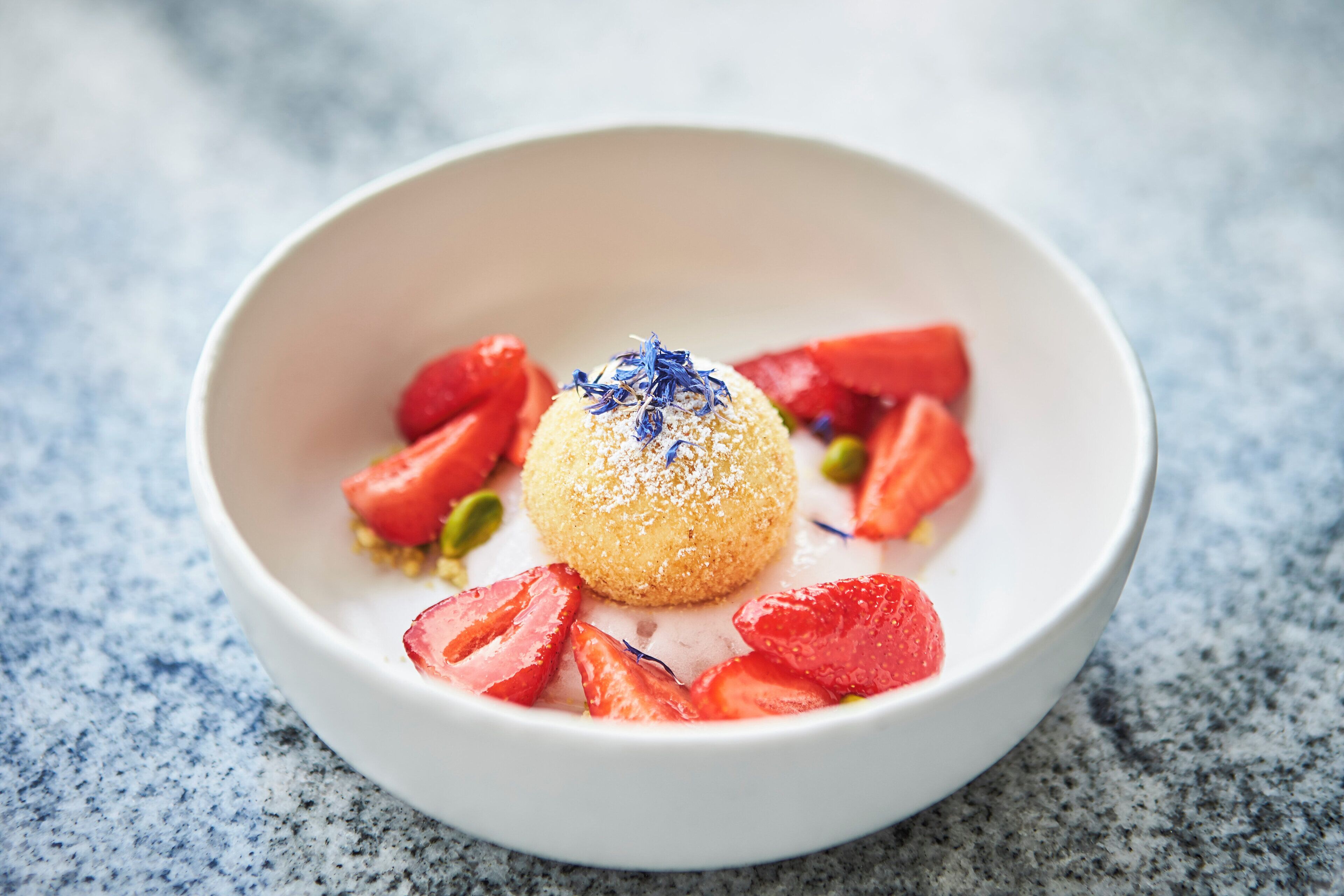 Un postre en un tazón blanco con fresas y un adorno azul.
