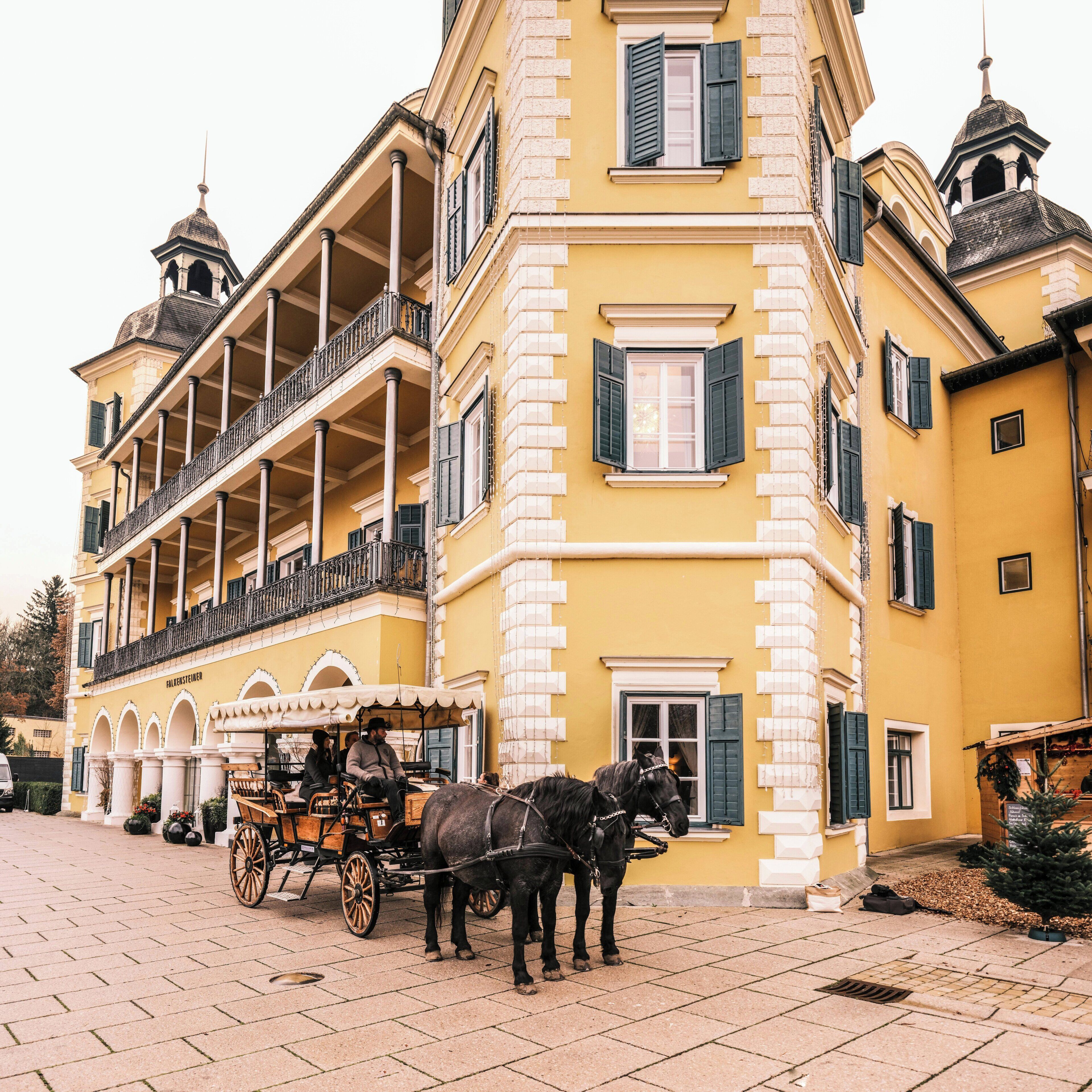 A yellow building with a balcony, a carriage, and horses.