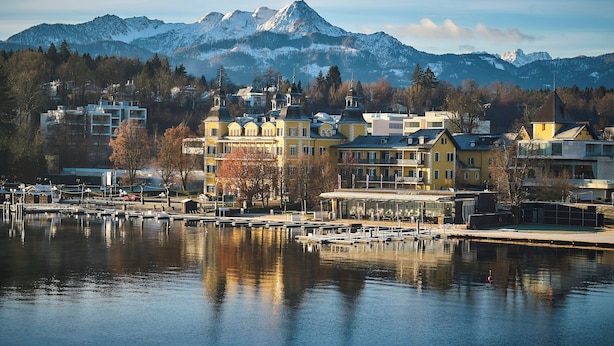 A lakeside town with buildings, a dock, and snow-capped mountains in the background.