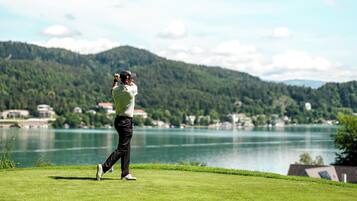 Players can tee off amidst a serene golf course landscape with a picturesque body of water and rolling hills in the background.