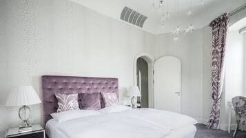 A neatly arranged bedroom with a large bed, a bedside table with a lamp, and a chair.