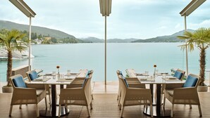 Una terraza con mesa y sillas que da a un lago, con montañas al fondo.