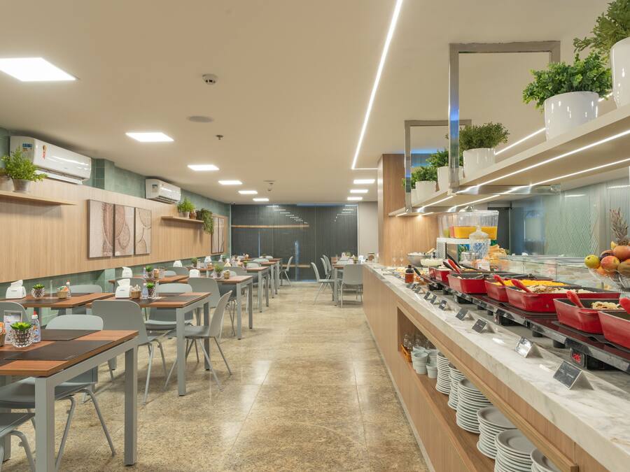 A modern dining area with multiple tables and chairs, a buffet with various food items, and air conditioning units on the walls.