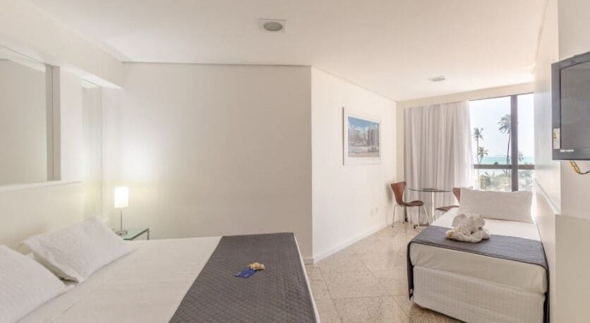 Habitación de hotel con cama, una mesita, una silla, televisor y ventana con vistas.