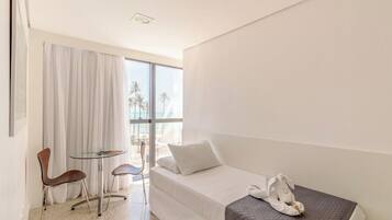 A hotel room with a bed, a small table with chairs, a window with curtains, and a view of palm trees.