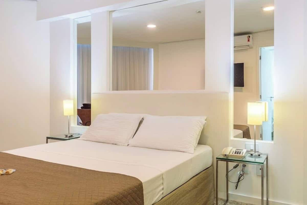 Una habitación de hotel con cama, lámparas de noche, teléfono y espejo.