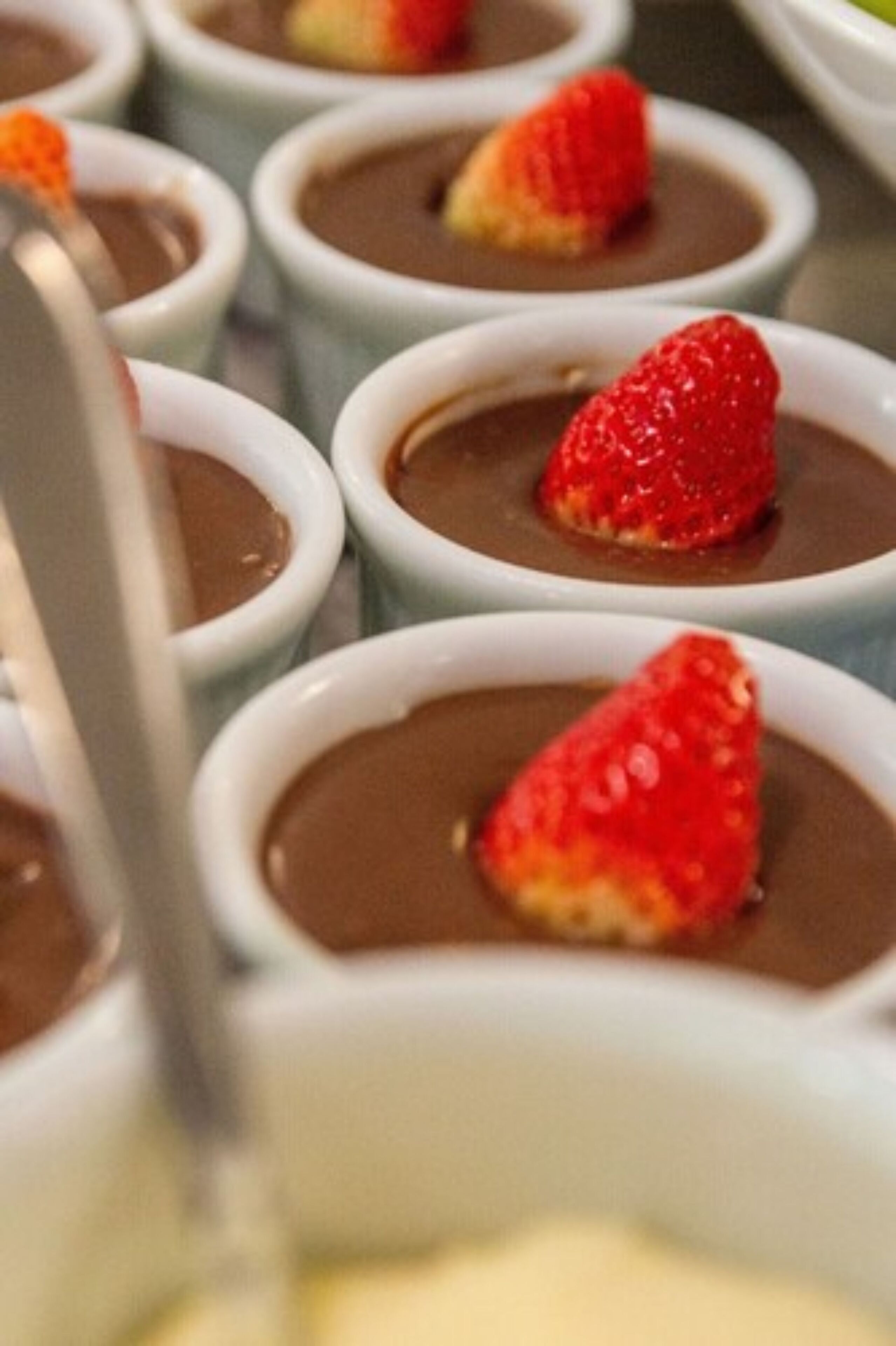 Una serie de recipientes blancos pequeños con postre de chocolate coronado con una fresa.