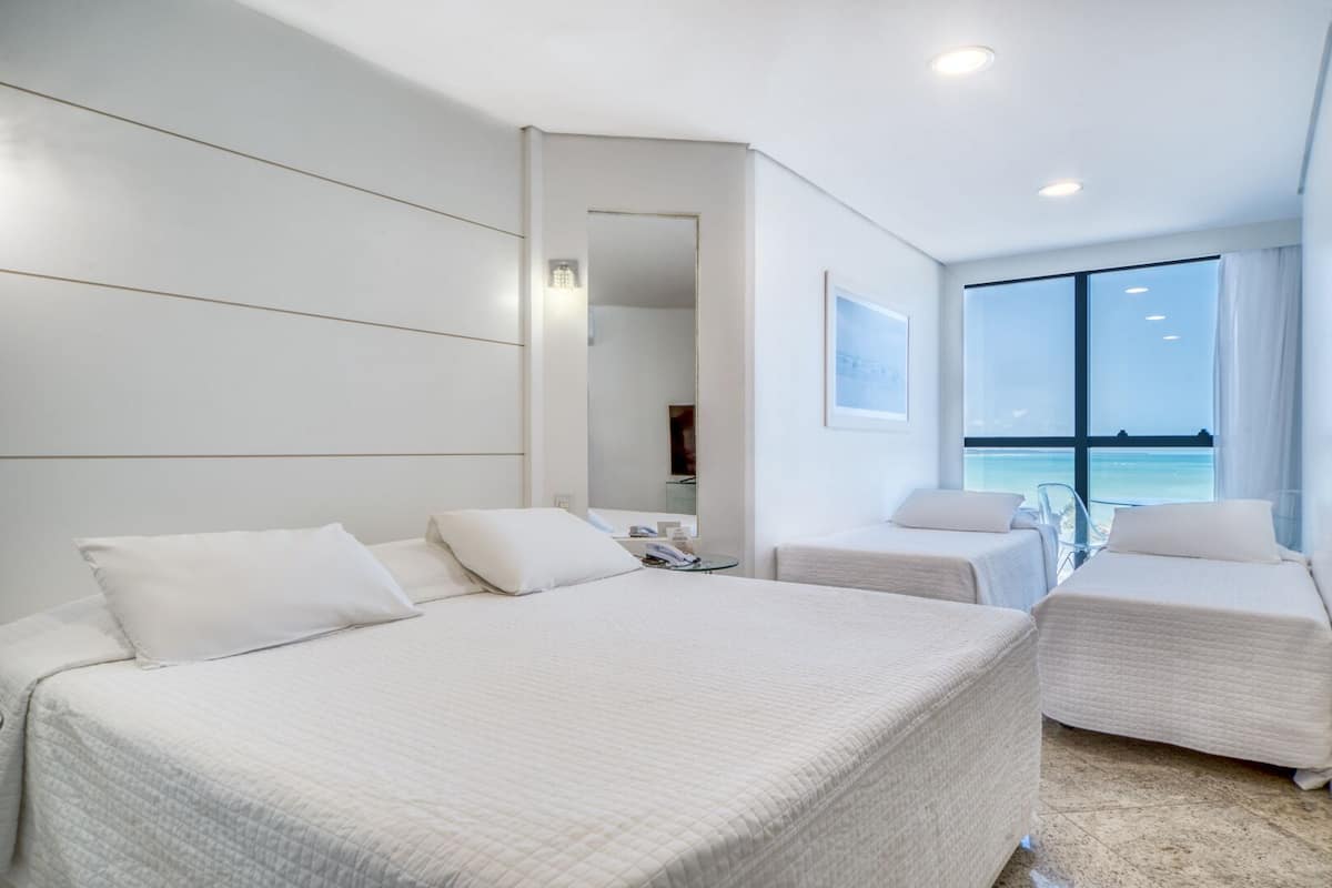 Habitación de hotel con una cama grande, dos camas más pequeñas, un escritorio y vista al océano.