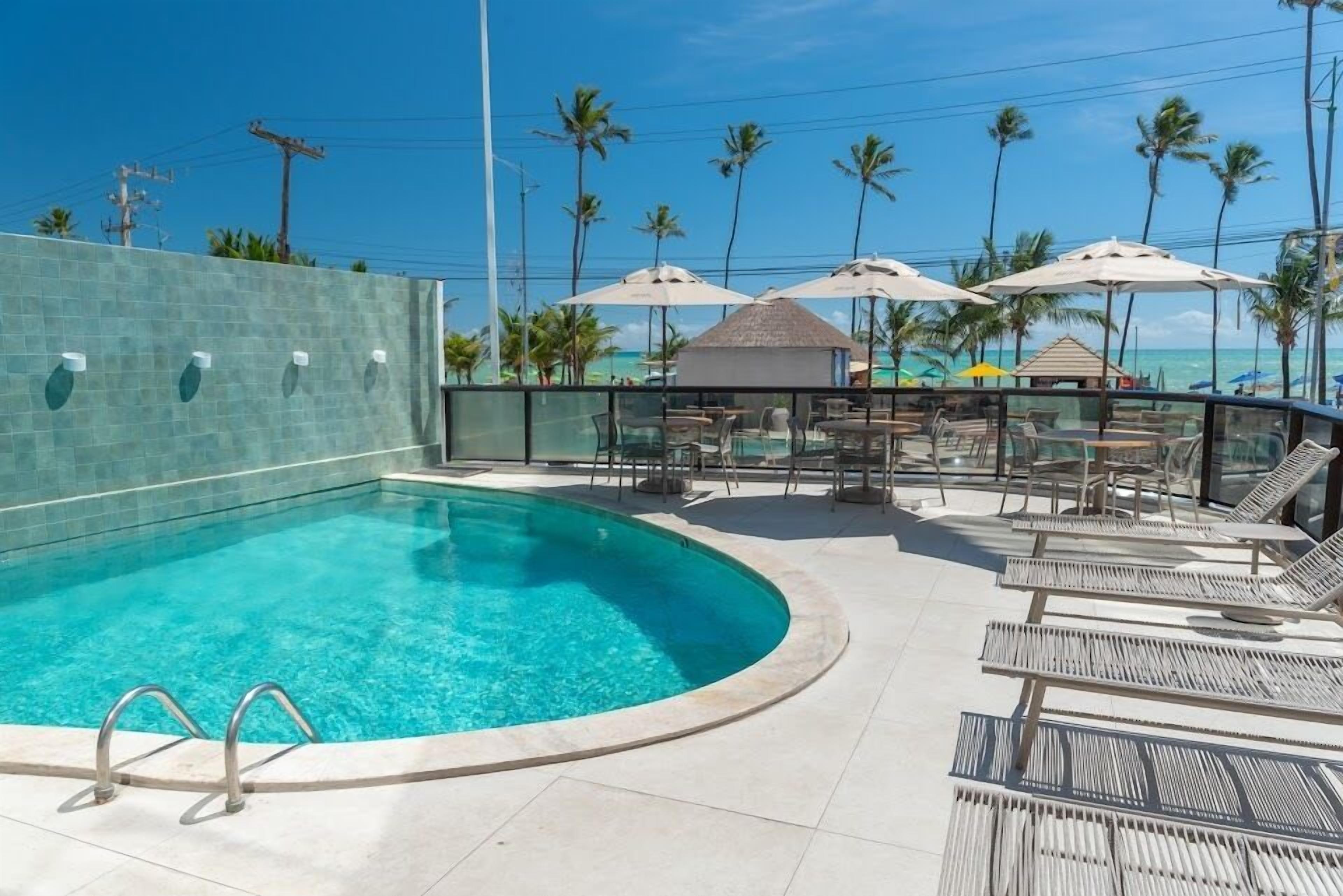 A swimming pool with lounge chairs and umbrellas, surrounded by palm trees and a clear sky.