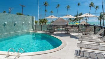 A swimming pool with lounge chairs and umbrellas, surrounded by palm trees and a clear sky.