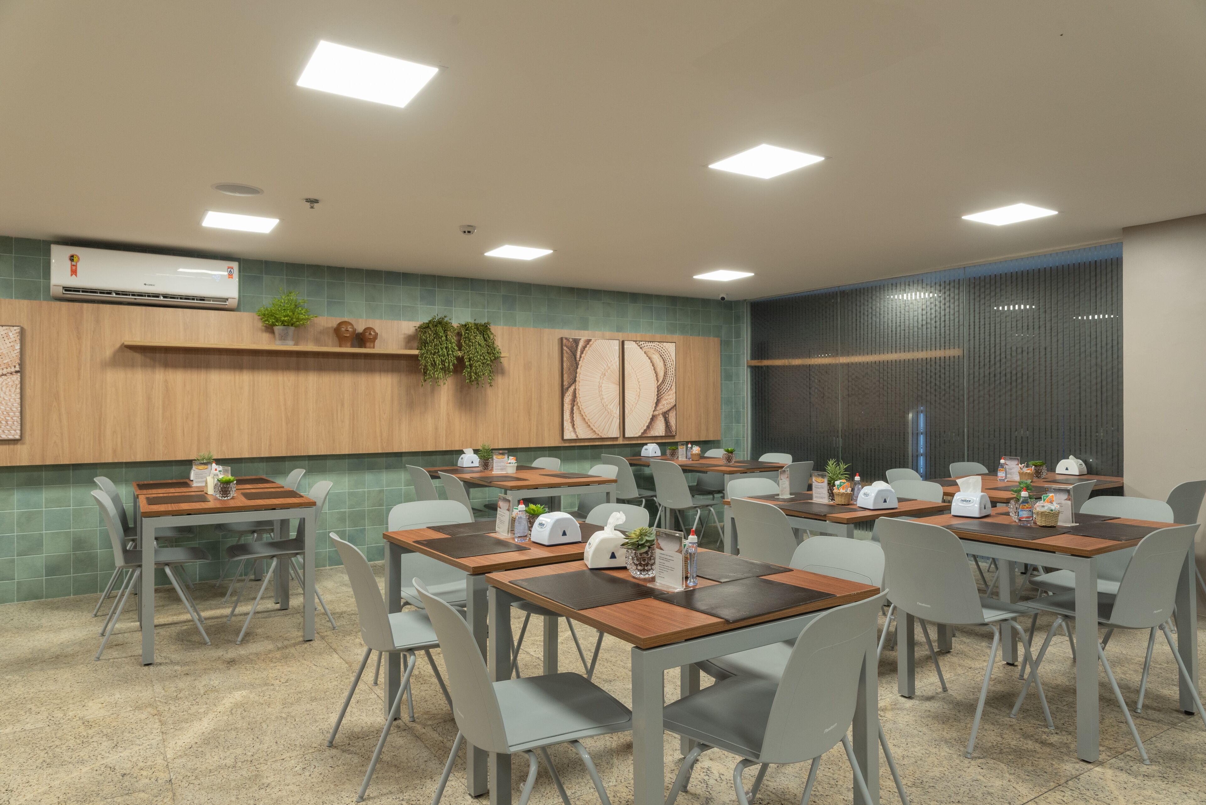 A modern conference room with multiple tables and chairs, equipped with air conditioning, plants, and a wooden accent wall.