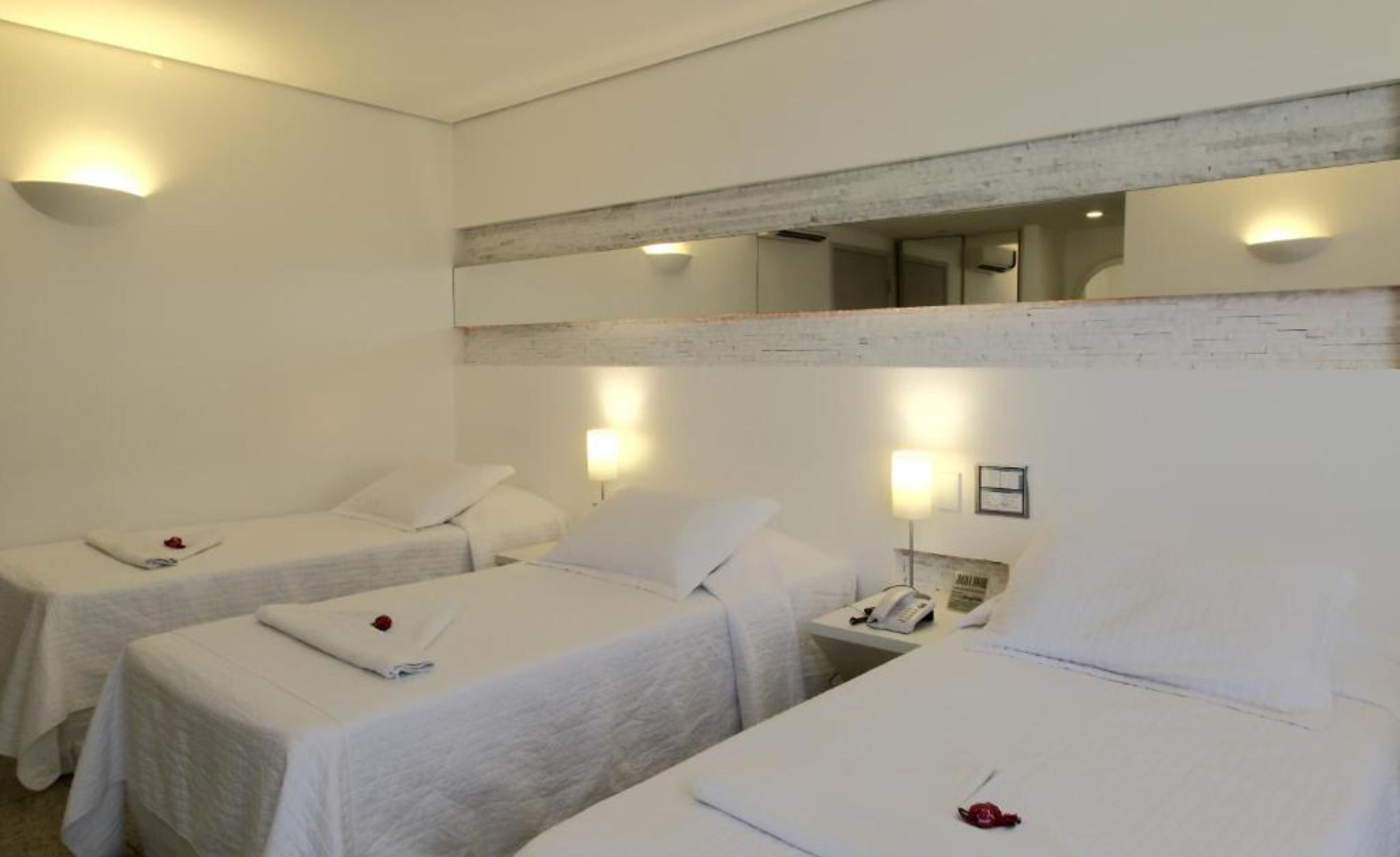 A hotel room with two single beds, a small bedside table with a lamp, and a mirror above the bed.