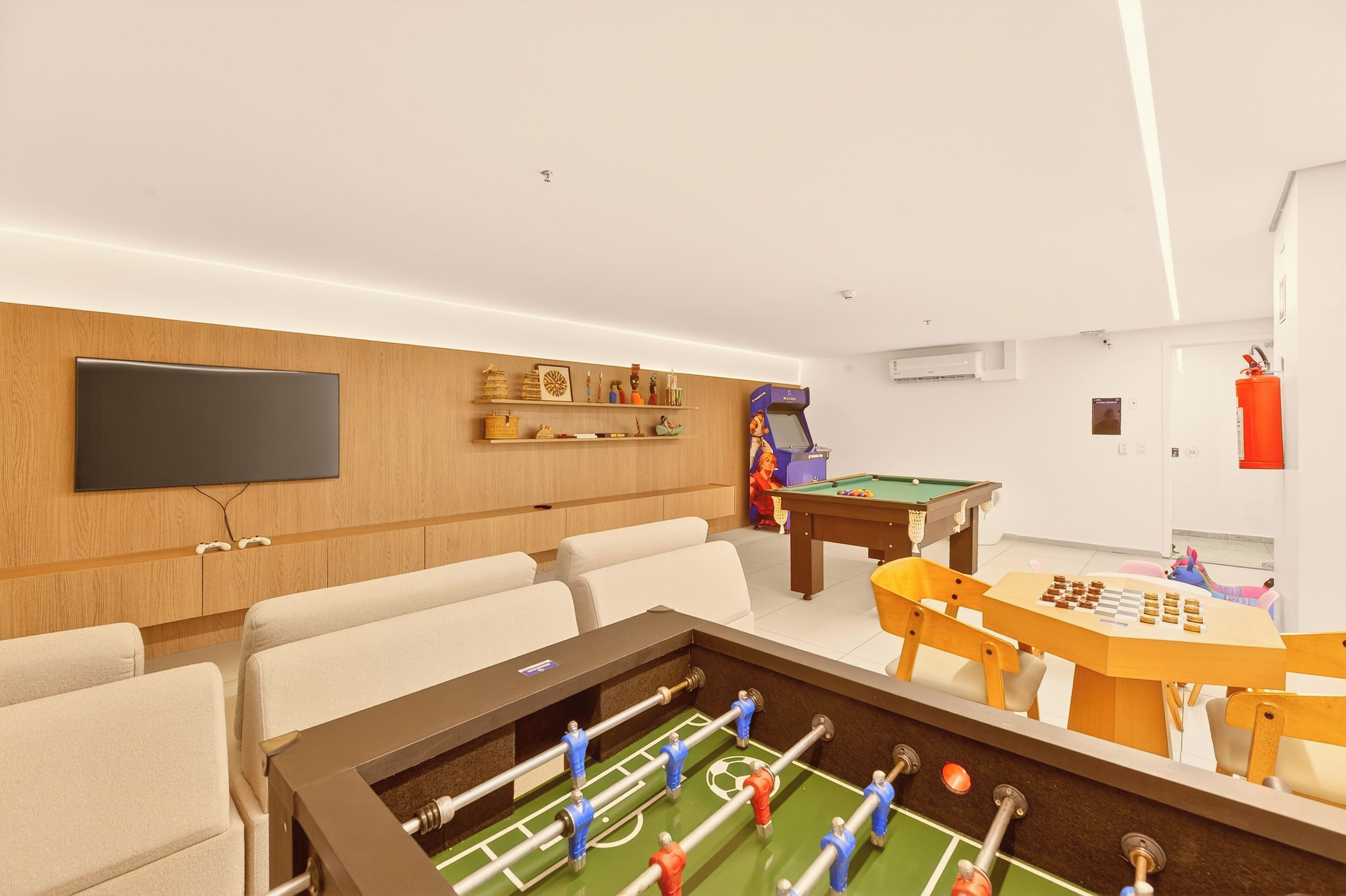 Una habitación con mesa de futbolín, mesa de billar y televisor montado en la pared.