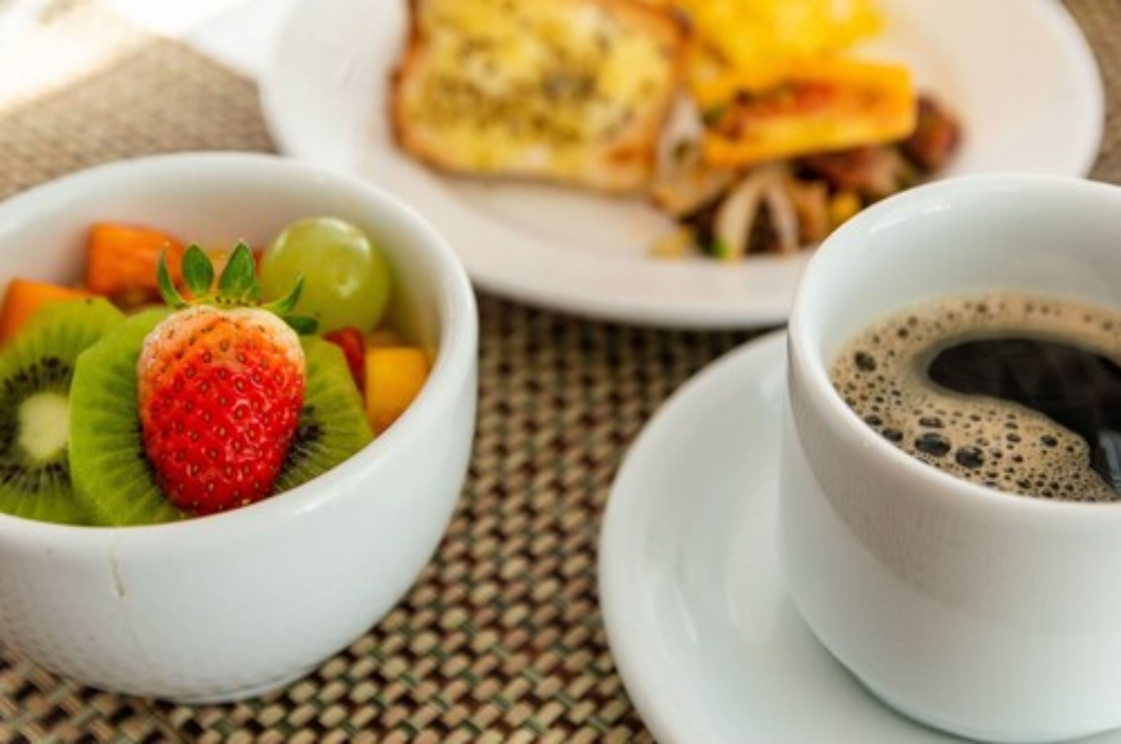 Un desayuno con un tazón de fruta, una taza de café y una tostada.