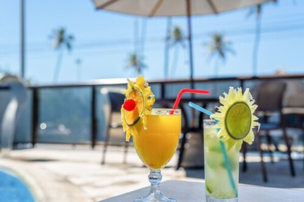 Two drinks on a table with a pool and palm trees in the background. - Hotel Brisa Tower Jatiúca (Maceió)
