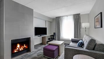 Une chambre d’hôtel moderne dotée d’une cheminée, d’un téléviseur à écran plat, d’un canapé, d’une petite table et d’une fenêtre avec des rideaux.