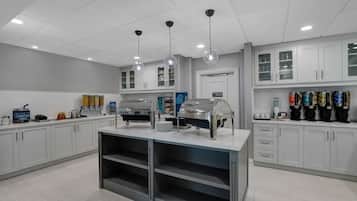 Una cocina moderna con armarios blancos, una isla central con estación para café e iluminación en el techo.