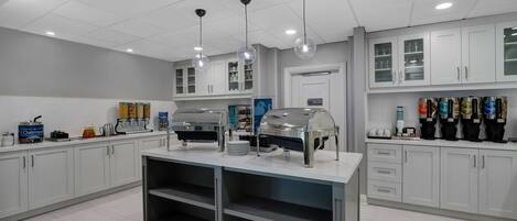 A modern kitchen with white cabinets, a central island with a coffee station, and overhead lighting.