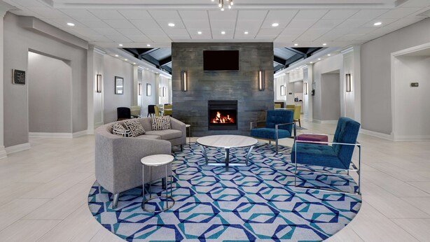 A modern lounge area with a fireplace, comfortable seating, and a patterned rug.