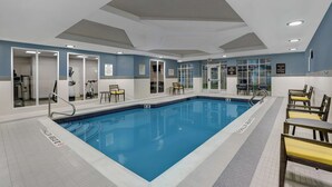 An indoor swimming pool with clear water, surrounded by seating areas and safety signs.