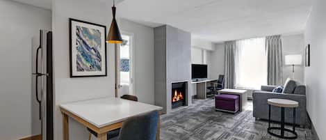 A modern living room with a fireplace, a dining area, and a seating area with a sofa and a small round table.