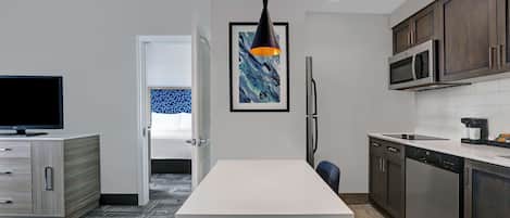 Une cuisine moderne avec un plan de travail blanc, des meubles en bois foncé, un luminaire suspendu noir et une œuvre d’art encadrée au mur.