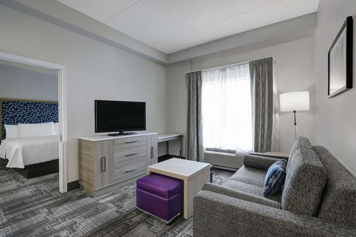 Ein Hotelzimmer mit Bett, Fernseher, Schreibtisch, Sofa und einem Fenster mit Vorhängen.
